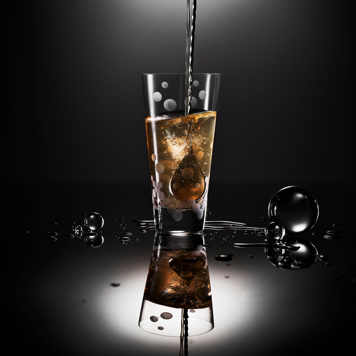 A glass of iced coffee is being poured into a Chatham Pop Highball Glass with a polka-dot pattern by Caskata.
