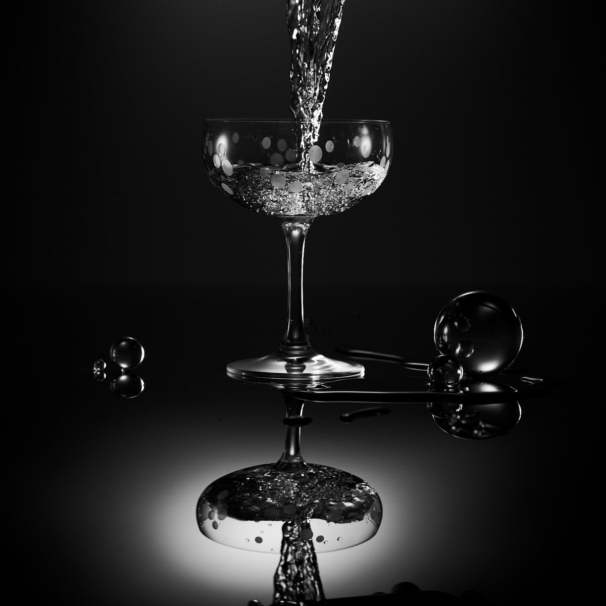 A Chatham Pop Coupe Cocktail Glass of water is being poured into a black background. (Caskata)
