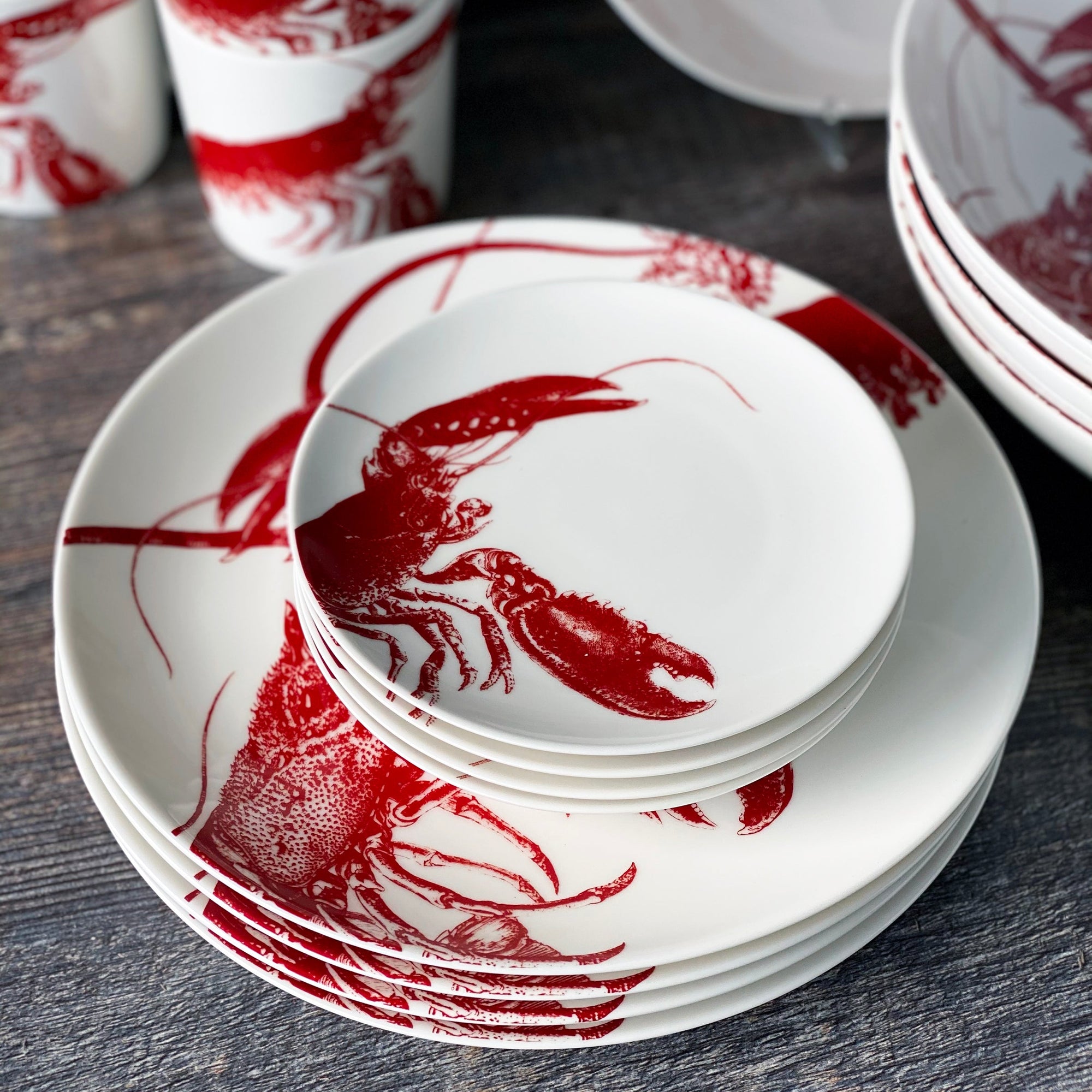 A set of Caskata Artisanal Home Complete Clambake 16 pc. Set plates with lobsters on them, perfect for a clam bake.
