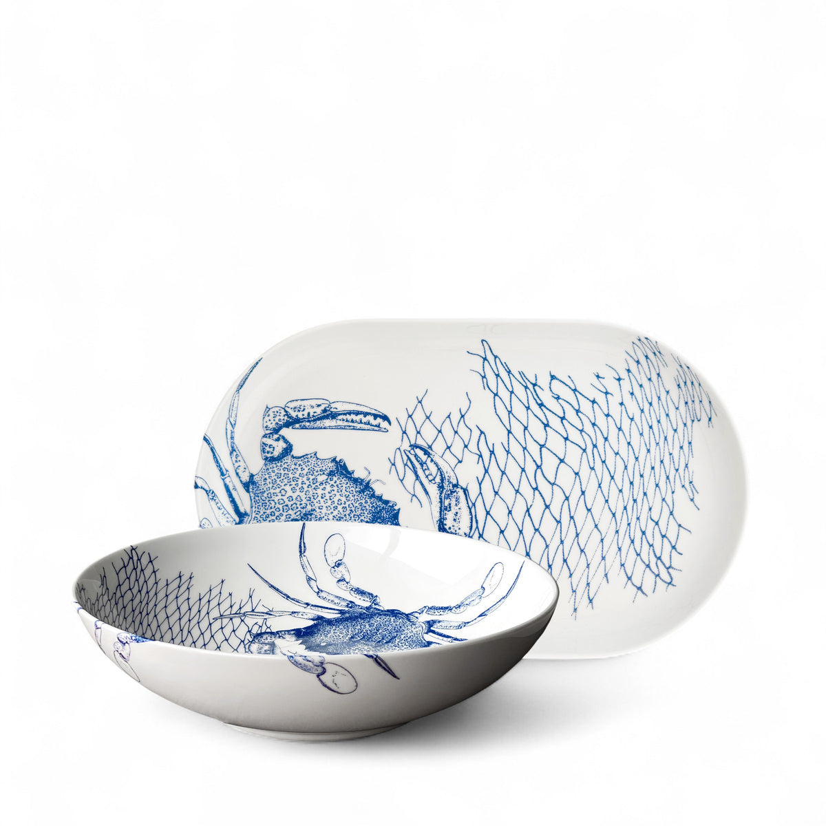 The Caskata Crab Serving Set includes a white ceramic bowl and platter with blue crab and fishing net designs—perfect coastal decor.