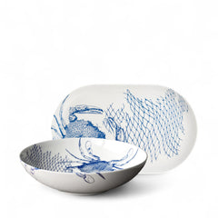 The Caskata Crab Serving Set includes a white ceramic bowl and platter with blue crab and fishing net designs—perfect coastal decor.