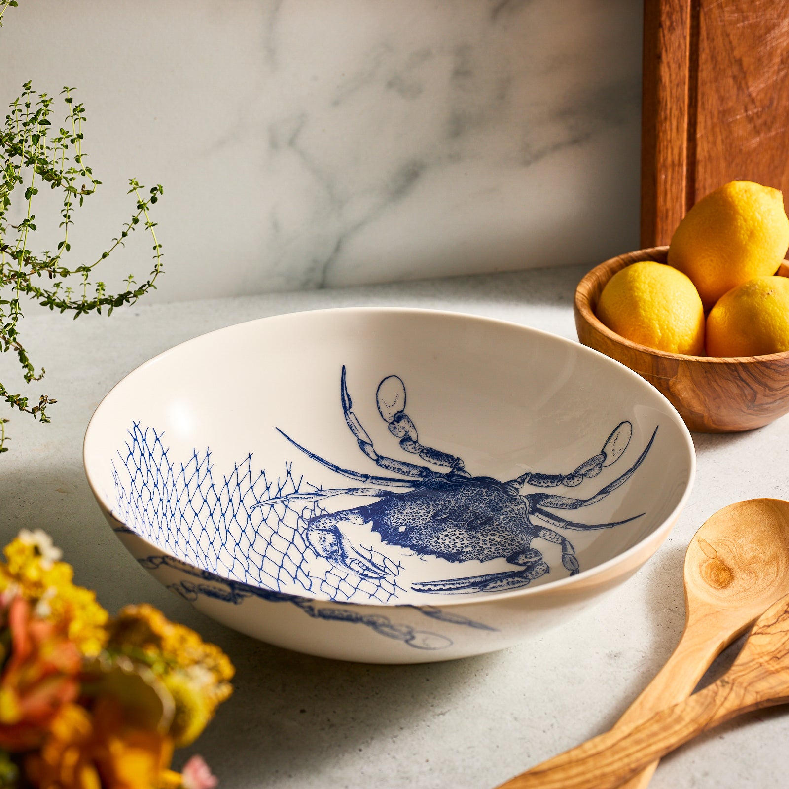 The Caskata Crab Serving Set includes a white ceramic bowl and platter with blue crab and fishing net designs—perfect coastal decor.