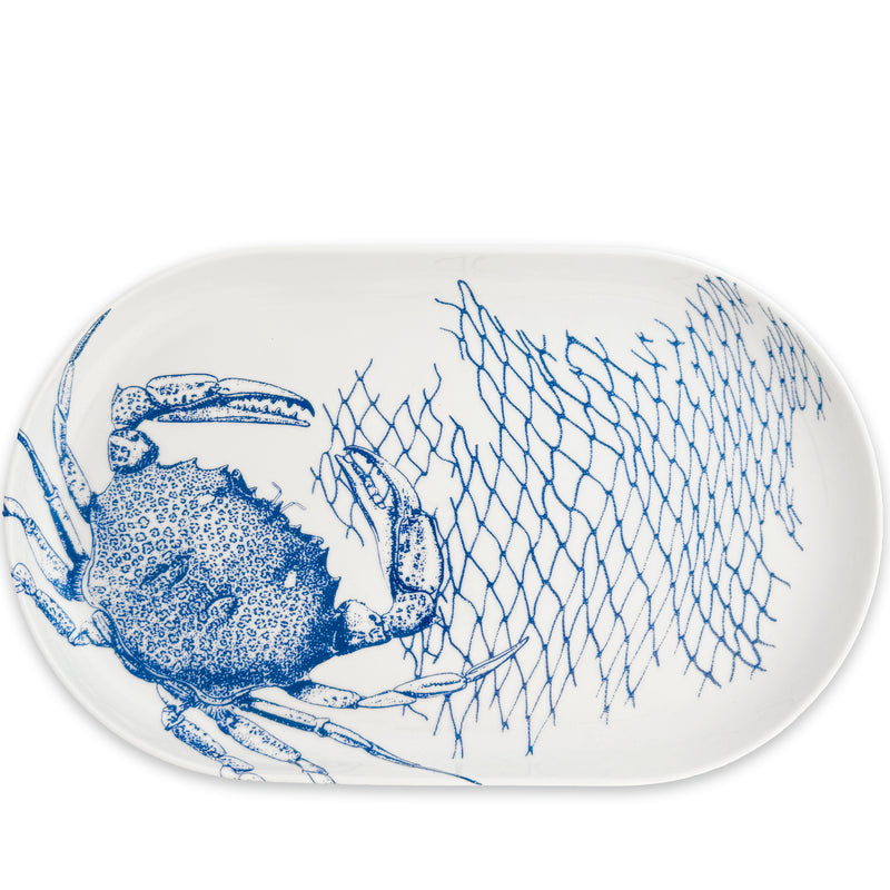 The Crab Large Coupe Oval Platter by Caskata features a charming blue illustration of a crab and fishing net design. Crafted from high-fired porcelain, this piece beautifully captures the crabs pattern, making it perfect for serving with style.