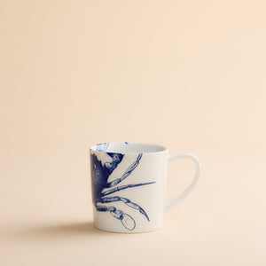 Caskata Artisanal Home’s Crab Mug—a white ceramic coastal mug adorned with a blue crab illustration—displayed on a simple beige background.