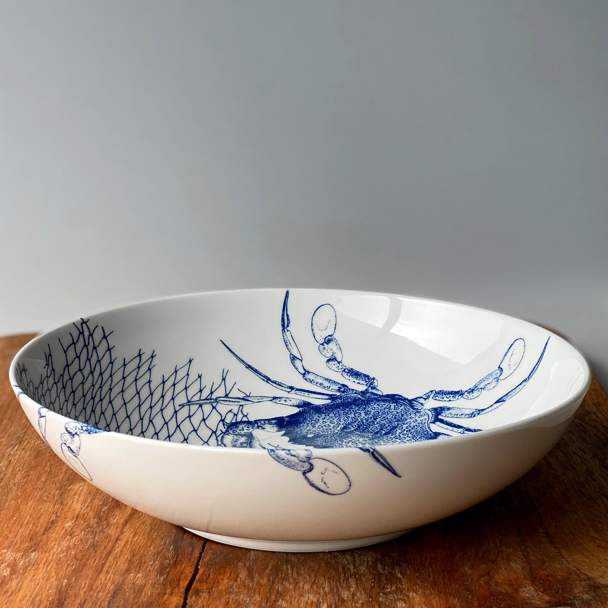 A blue and white Crab Wide Serving Bowl with a crab design, dishwasher and microwave safe, made by Caskata Artisanal Home.