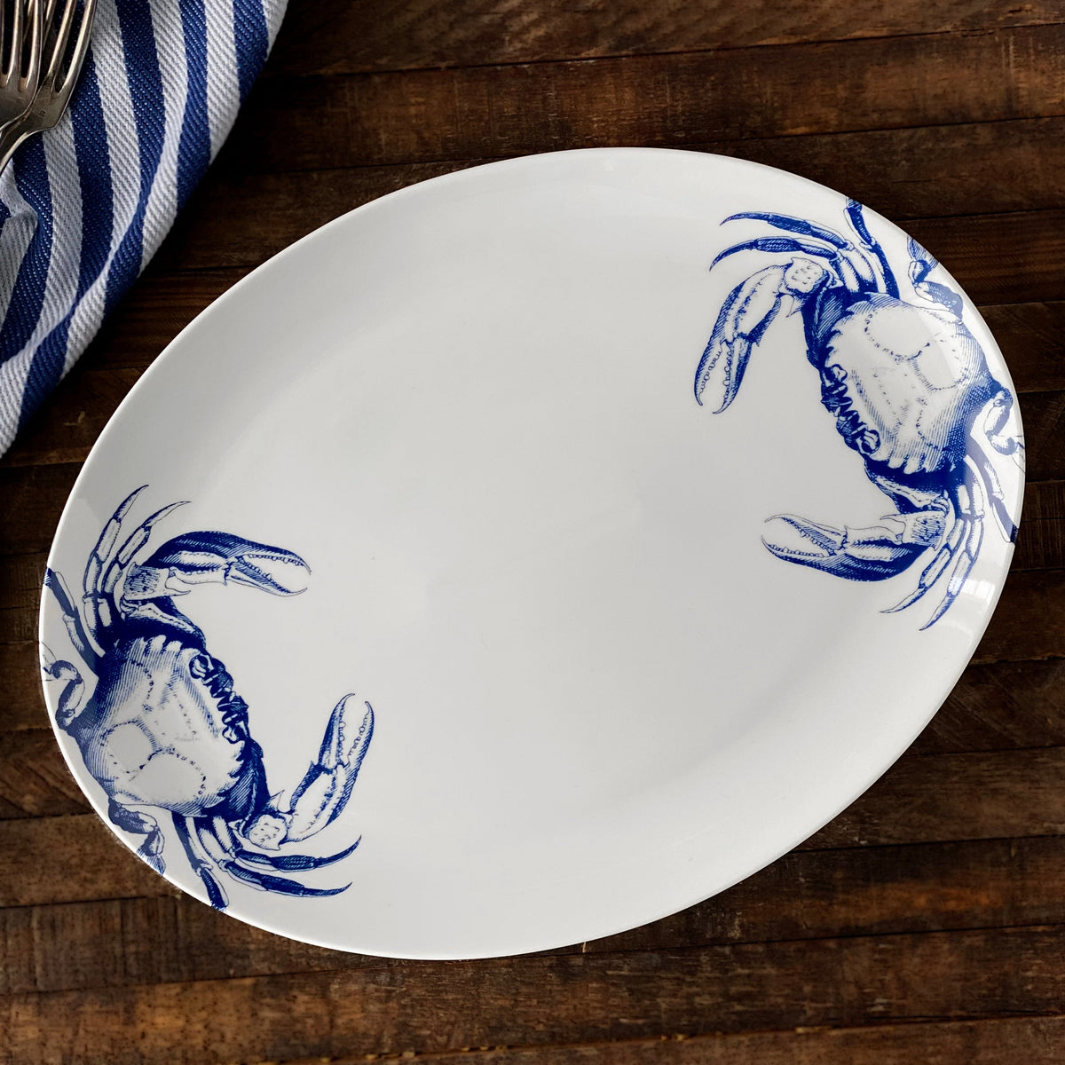 A Crab Coupe Oval Platter with a crab on it, perfect for coastal style decor, made by Caskata Artisanal Home.