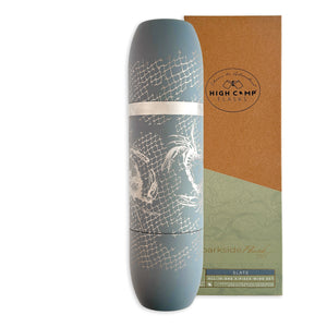 A Caskata x High Camp Dark Gray Crabs & Nets Wine Flask, featuring a white etched design and magnetized cups for easy use, is displayed standing next to its cardboard packaging.