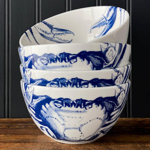 A stack of five Caskata Crab Cereal Bowls featuring a crabs pattern sits on a wooden surface against a black paneled background.