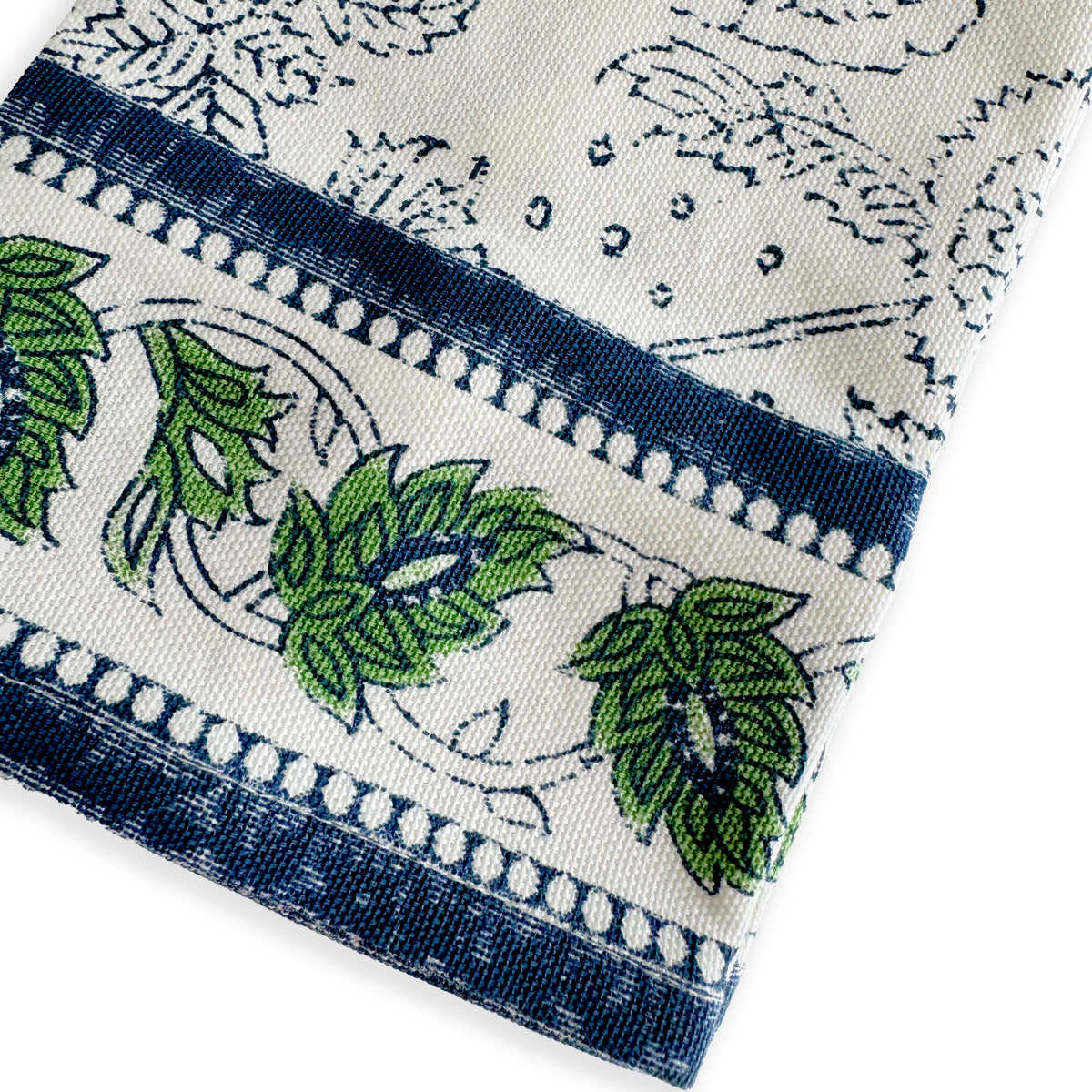 A close-up of Caskata's Cuttyhunk Block Print Dinner Napkins, featuring a white cotton napkin with blue borders and a green leaf pattern—perfect for adding bohemian flair and unique style to your table.