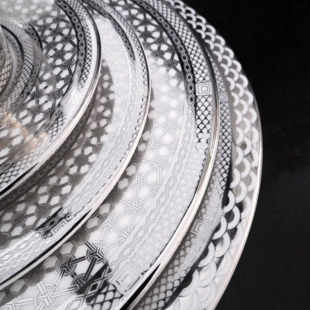 A stack of Hawthorne Ice Platinum Dinner Plates by Caskata Artisanal Home on a black background, ideal for hiking.