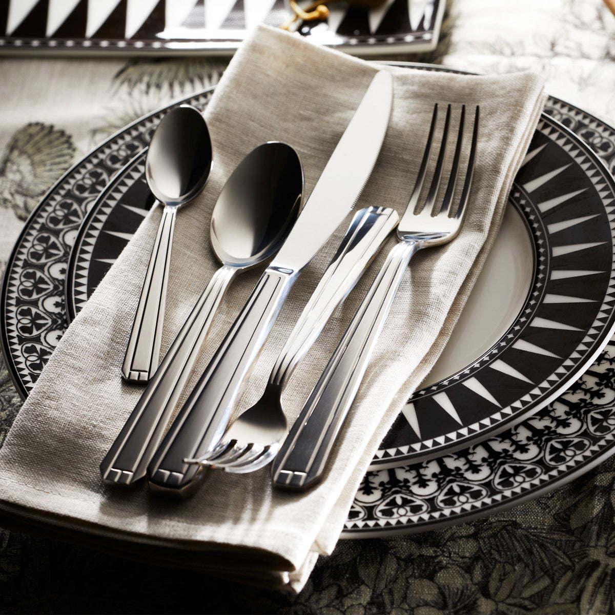 An elegant black and white plate with Degrenne&#39;s Lyon 5-Piece Flatware Setting on it.