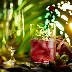 Sand etched mixing glass beaturing red cocktail with a tropical background.