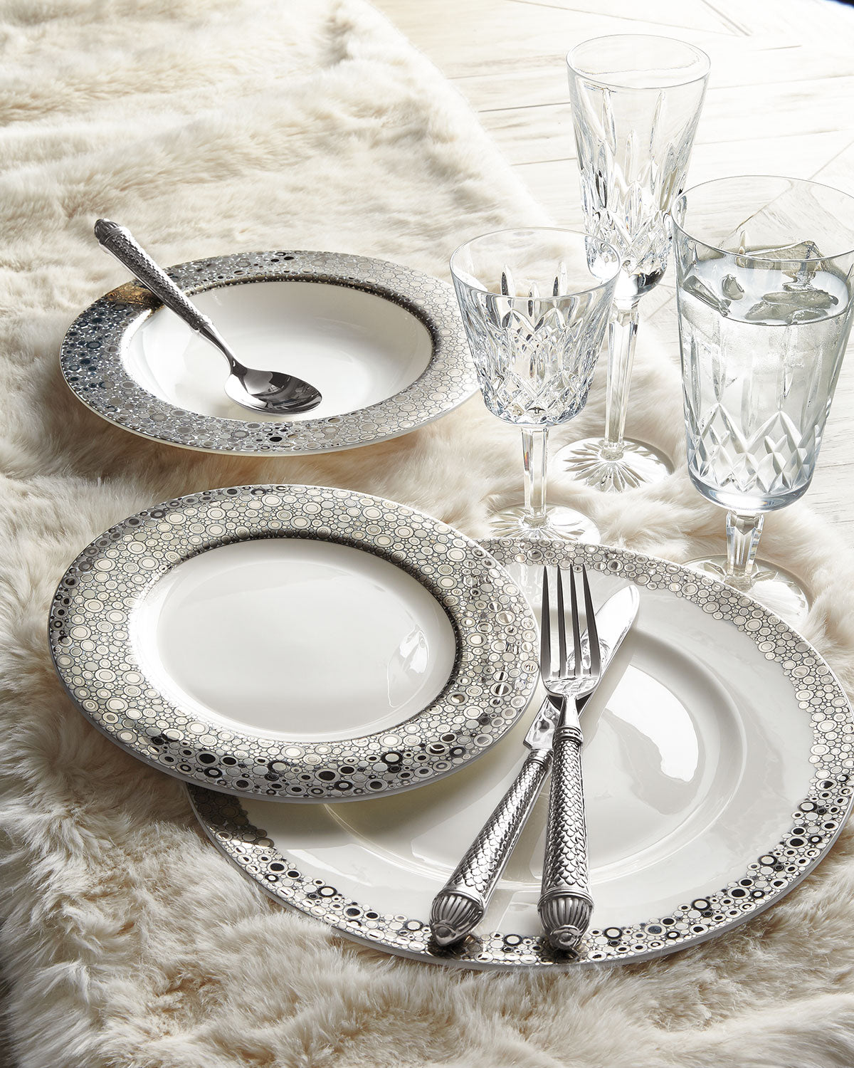 A Caskata Artisanal Home Ellington Shine Platinum Rimmed Soup Bowl and silverware on a white rug, suitable for traveling or camping.