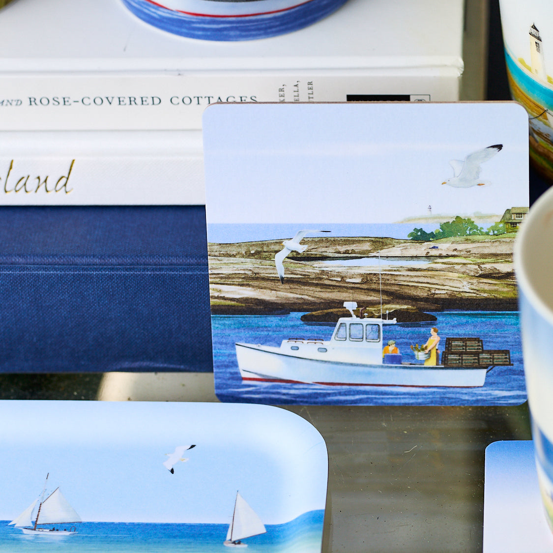 The Caskata X Felix Doolittle Summer Birchwood Coasters, Set of 4, features a fishing boat, lobster traps, and seagull on blue water with a rocky shore—capturing classic New England charm.
