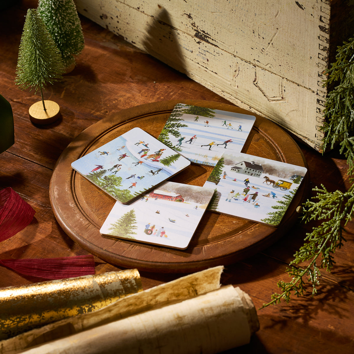 The Caskata X Felix Doolittle Winter Birchwood Coasters, Set of 4, by Caskata features sustainable coasters with winter scenes, arranged on a birchwood tray—an eco-friendly holiday accent. Made in Finland.