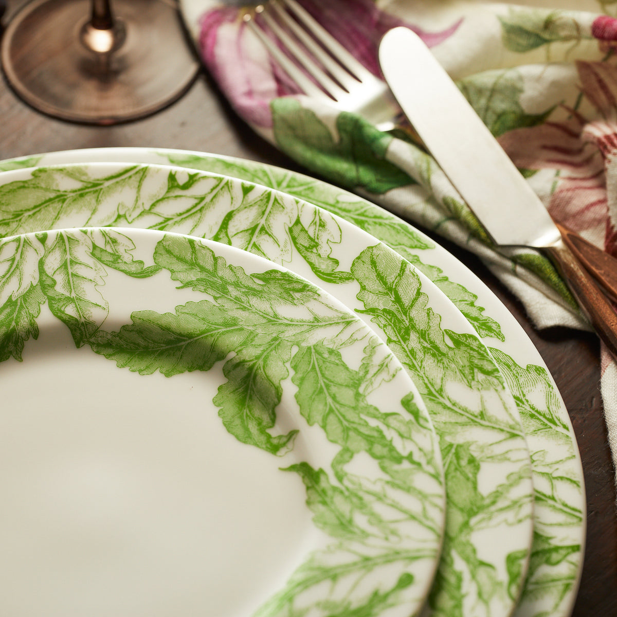 A Freya Rimmed Salad Plate by Caskata Artisanal Home with green leaves and a fork on a table made of porcelain.