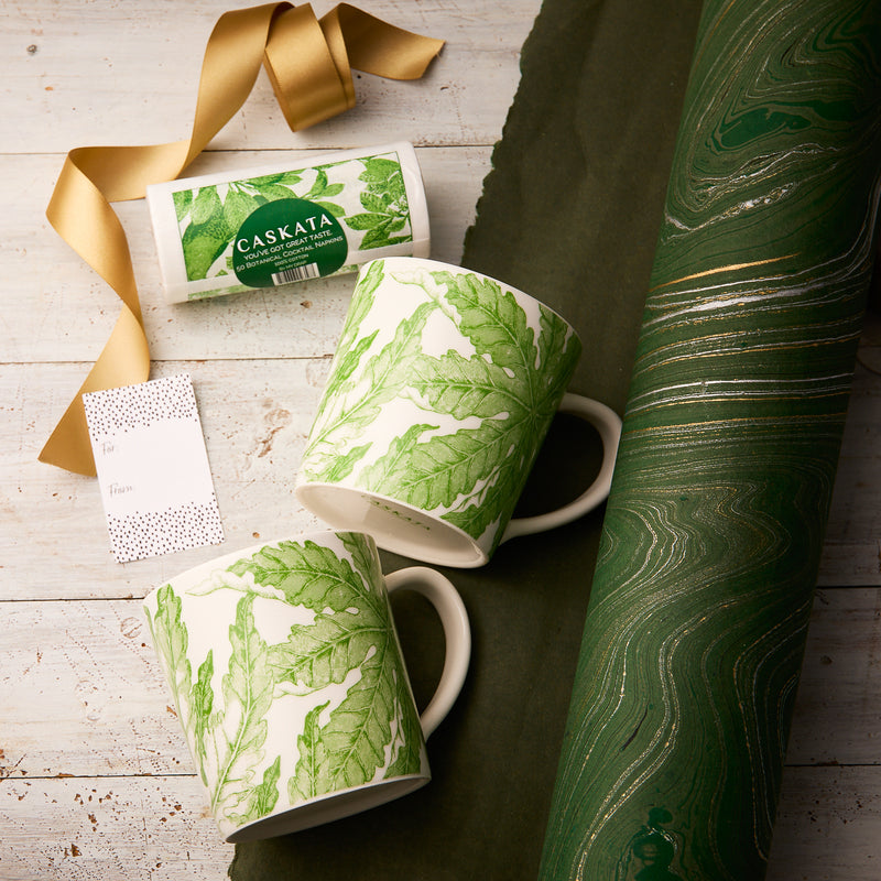 The "Freya Coffee Talk" Bundle by Caskata features two white porcelain mugs with green leaf designs, a card, and elegant wrapping—perfect for gifting to nature lovers.