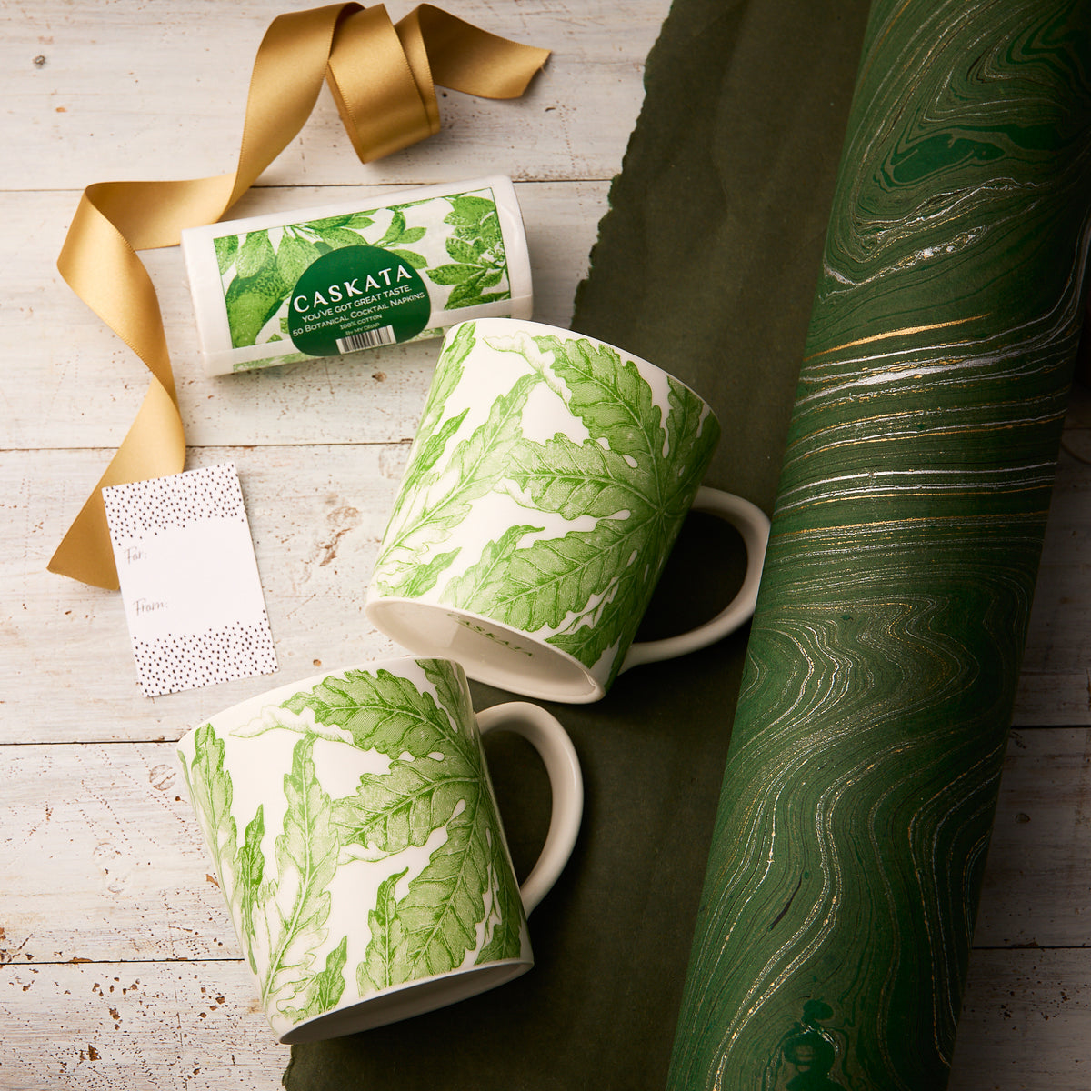 The "Freya Coffee Talk" Bundle by Caskata features two white porcelain mugs with green leaf designs, a card, and elegant wrapping—perfect for gifting to nature lovers.
