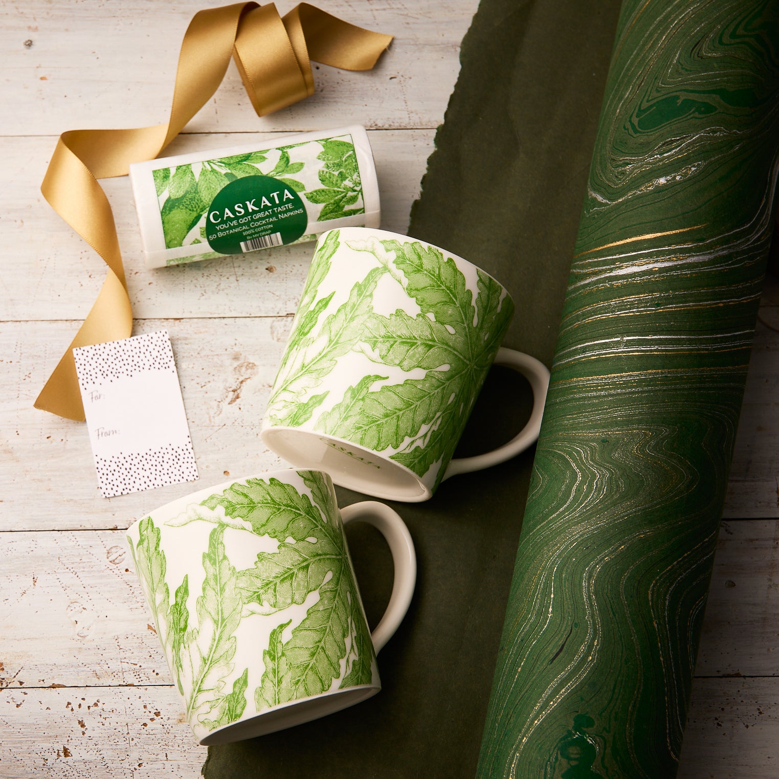 The "Freya Coffee Talk" Bundle by Caskata features two white porcelain mugs with green leaf designs, a card, and elegant wrapping—perfect for gifting to nature lovers.