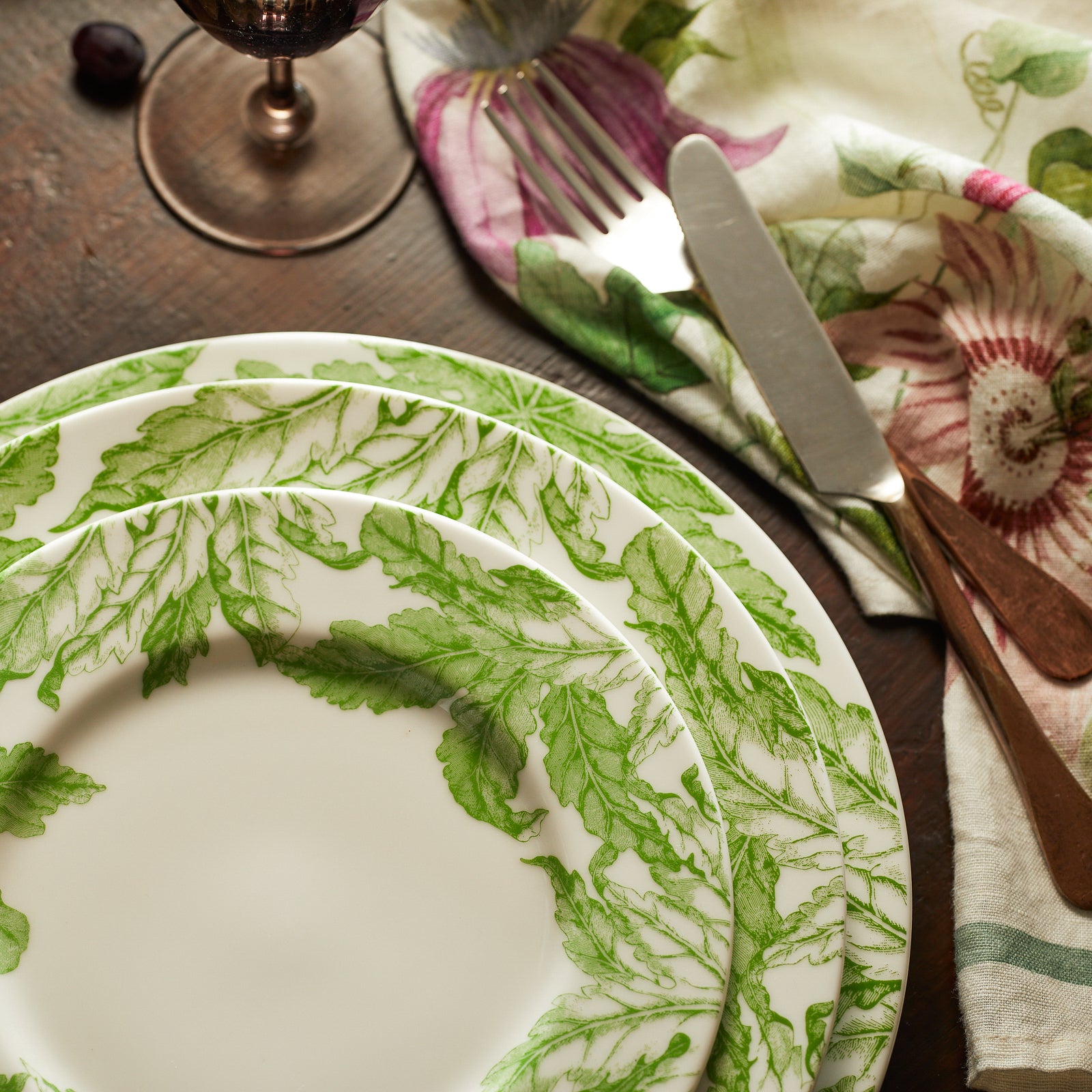 The Caskata Freya Ultimate Set is a 42-piece porcelain dinnerware collection with plates, bowls, and mugs in a green leafy pattern on white. Dishwasher and microwave safe, it's beautifully arranged on a white surface.