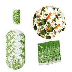 The Gardener's Deluxe Bundle by Caskata includes green fern-patterned porcelain salad plates, botanical cocktail napkins, a vase, and a round plate with orange flowers and green vines.