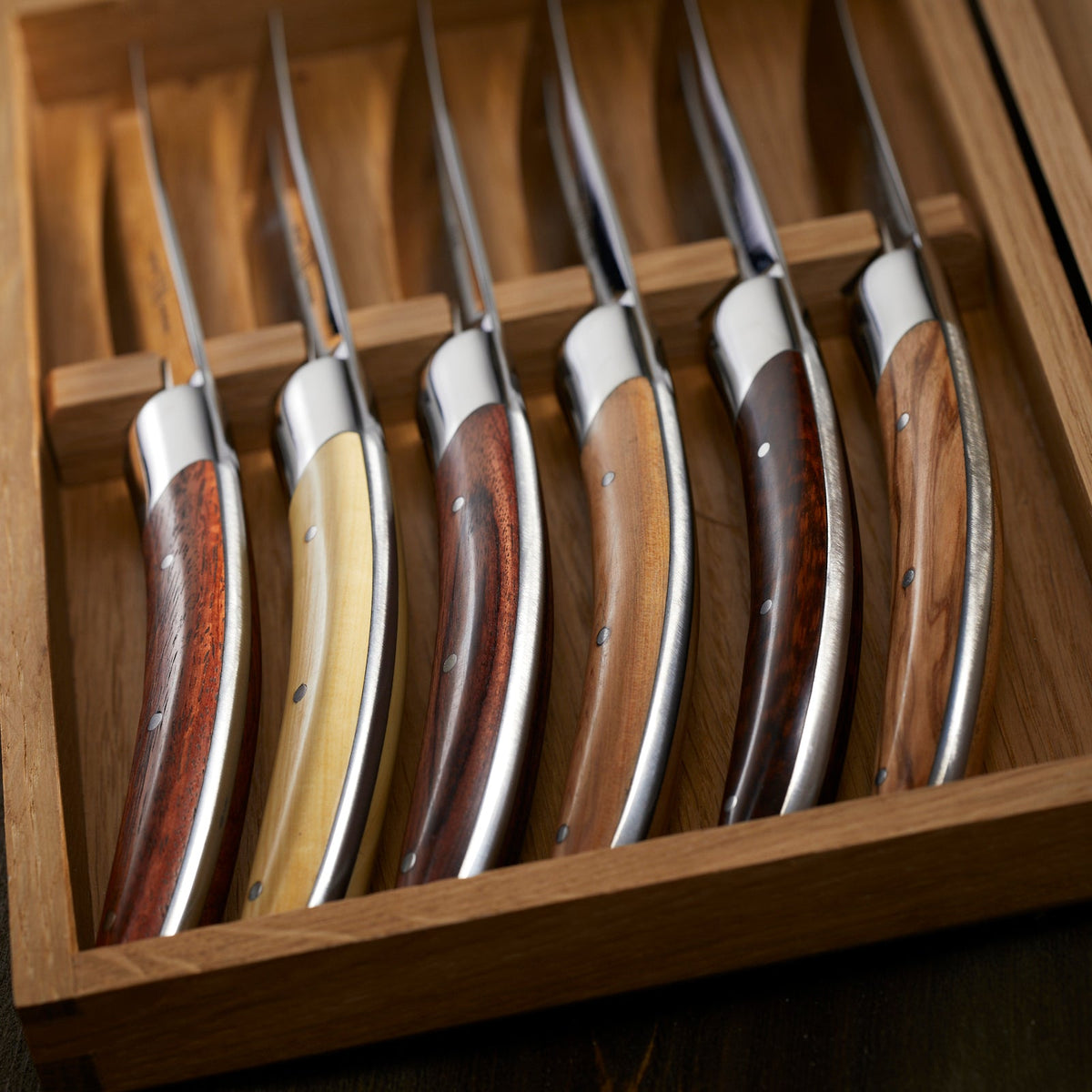 A set of Goyon-Chazeau Styl&#39;ver Mixed Wood Steak Knives Boxed Set/6 in a wooden box.