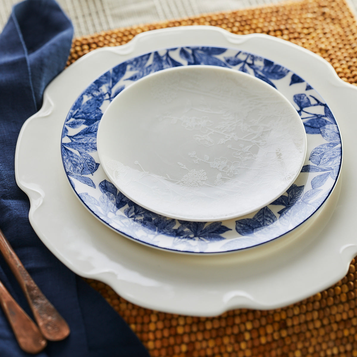 A Grace White Dinner Plate from Caskata Artisanal Home sits elegantly on a table, showcasing its polished curves.