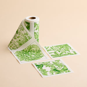 A roll of the MY DRAP Botanicals Verde Cocktail Napkin Roll, featuring green botanical designs, is partially unrolled with three square sections displayed flat on a beige surface—showcasing the fresh elegance typically found in floral cocktail napkin patterns.