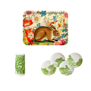 The Green Bunnies Bundle by Caskata includes a birchwood tray with a brown rabbit, a leaf-wrapped napkin, and four white plates with green bunny motifs—an ideal eco-friendly set for spring gatherings.
