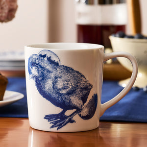 The Caskata Grumpy Chick Mug features a white porcelain body with a blue chick and partial sun or moon illustration, adding fun to your morning routine. Perfect for breakfast, this drinkware brings charm to your table.