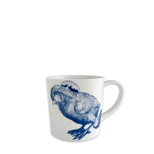 The Caskata Grumpy Chick Mug is a white high-fired porcelain mug featuring a detailed blue illustration of a grumpy chick with its head down and a circular background design.