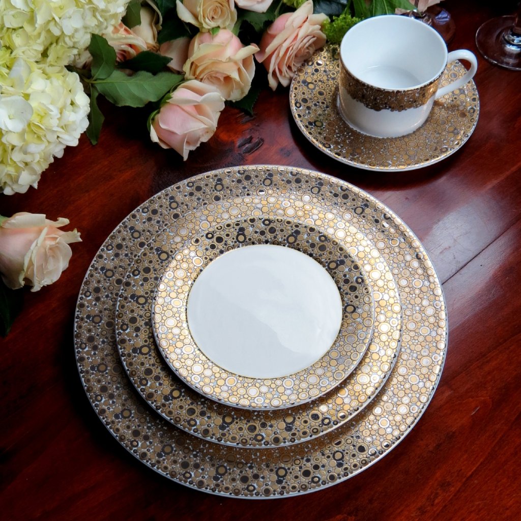 A table setting with a Caskata Artisanal Home Ellington Shimmer Gold &amp; Platinum 5-Piece Place Setting on a wooden table.
