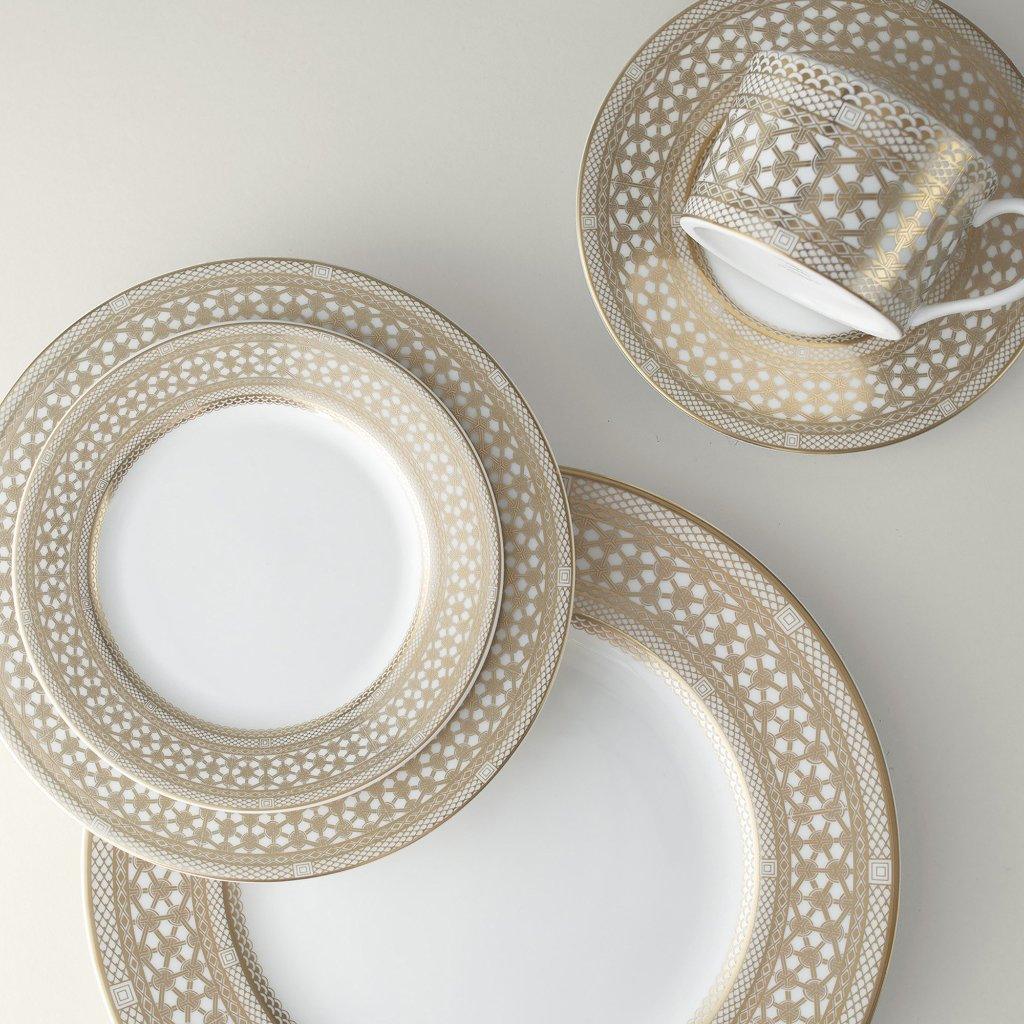 A set of four Hawthorne Gilt Cup &amp; Saucer from Caskata Artisanal Home, featuring intricate gold and white patterns reminiscent of filigree jewelry, arranged on a white surface.