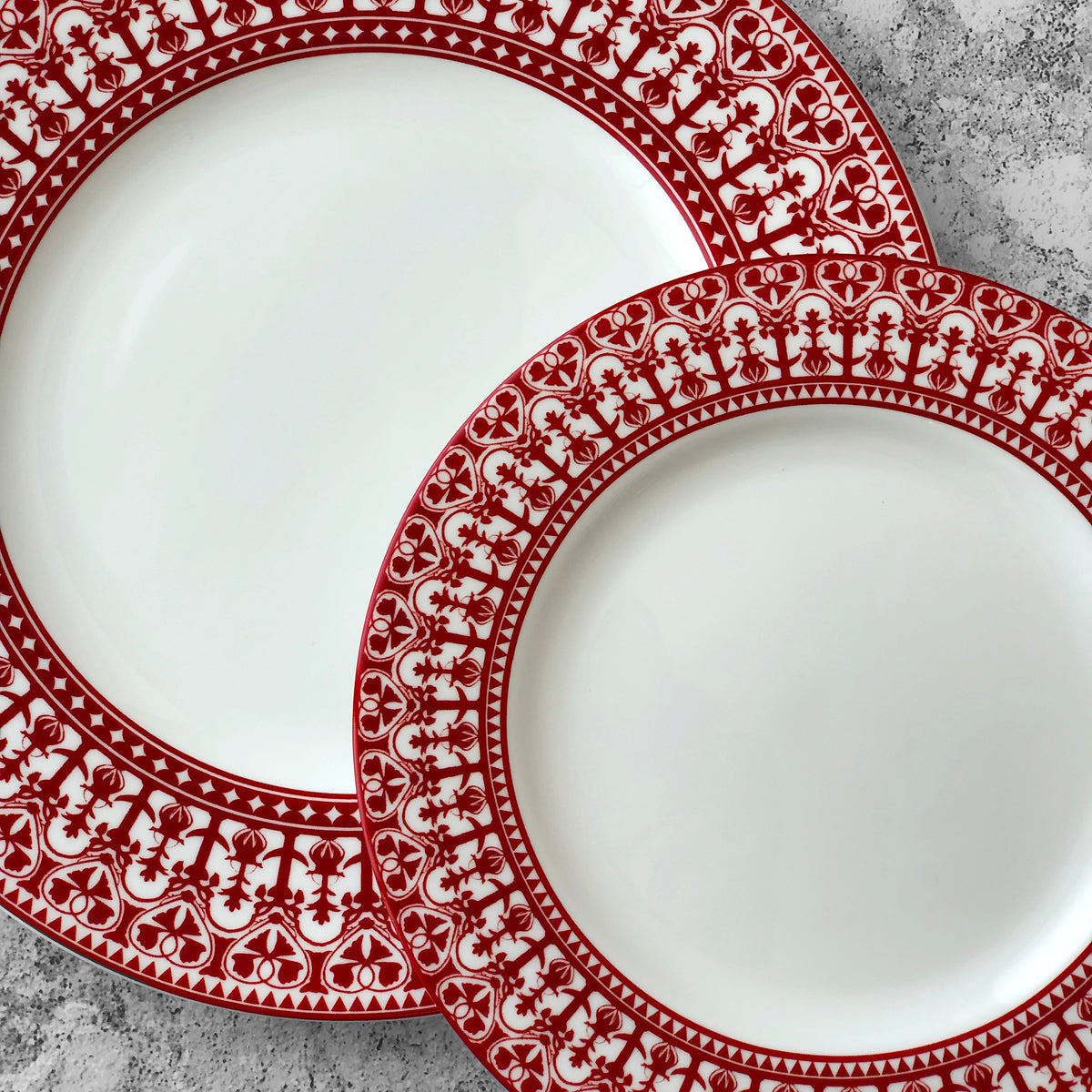 Two Casablanca Crimson Rimmed Dinner Plates by Caskata Artisanal Home on a concrete surface.