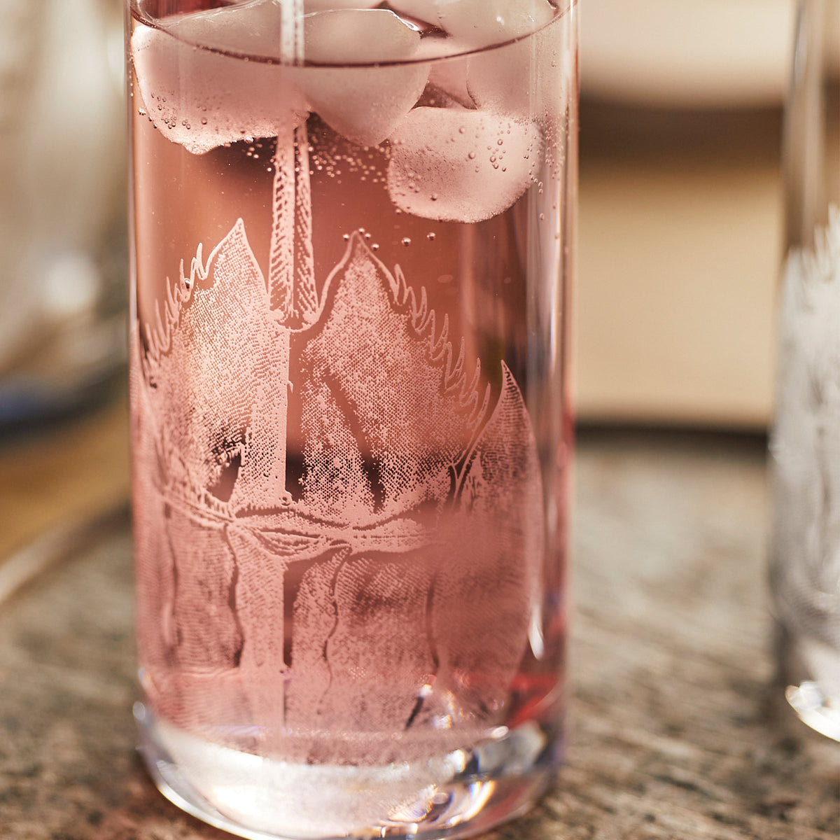 A Caskata Horseshoe Crab Highball Glass filled with a pink liquid and ice.