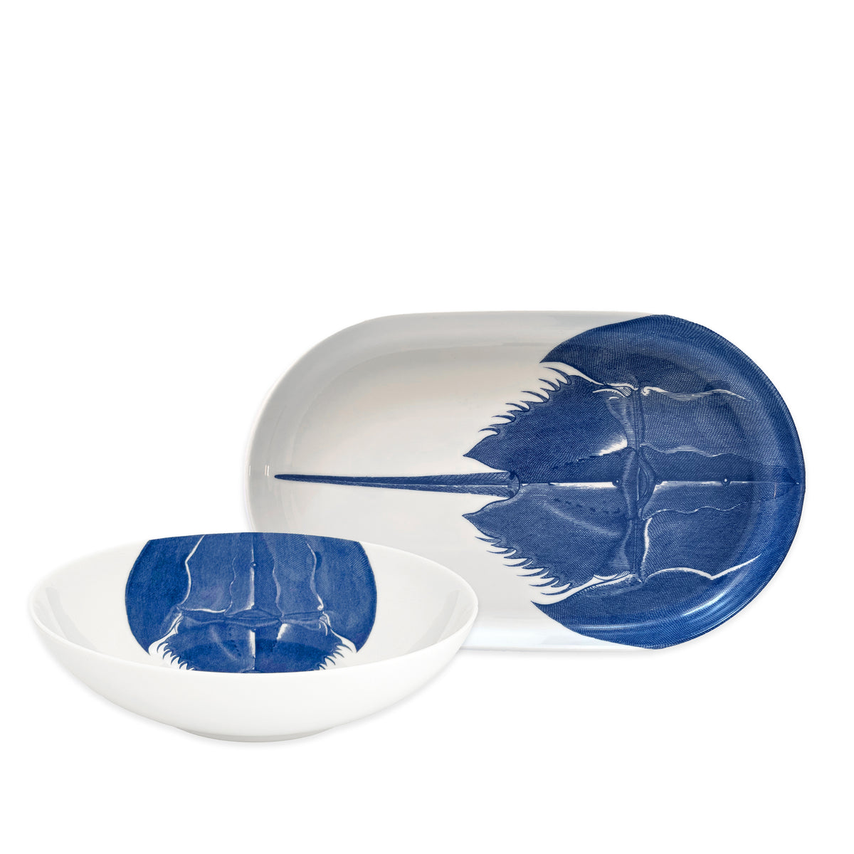 The Caskata Horseshoe Crab Serving Set features a white ceramic bowl and oval platter, each decorated with a blue horseshoe crab—making it an ideal and unique housewarming gift.
