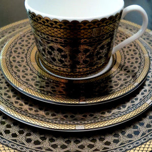 A black and gold Hawthorne Onyx Gold & Platinum Bread & Butter Plate by Caskata Artisanal Home on a table, perfect for luxurious tea or coffee moments.
