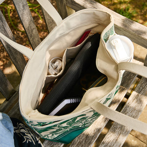 The Caskata x Steele Everyday Tote Bag Arbor Green by Caskata, handcrafted in the USA, sits on a bench filled with essentials like a water bottle, tablet, notebook, cable, pen, and pouch.