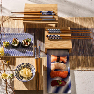 The Japanese food set includes sushi and nigiri artfully arranged on Caskata's Newport Petite Trays, Set of 2, complemented by pickled ginger and wooden chopsticks, all elegantly presented on decorative plates and mats.
