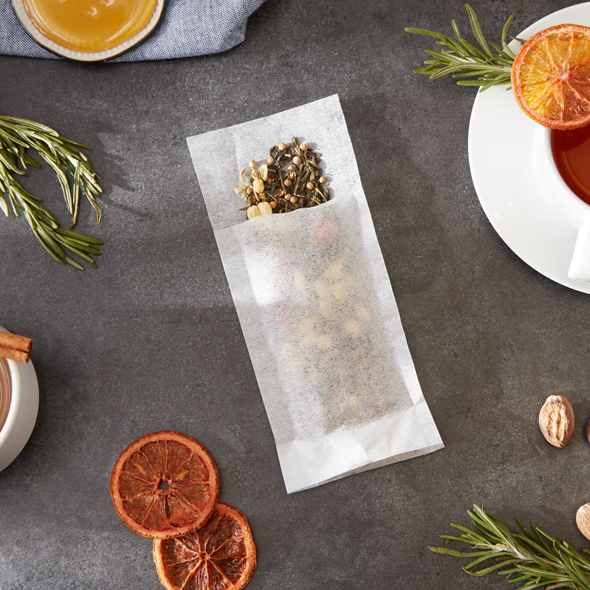 A bag of Large Tea Filters from RSVP International with cinnamon sticks and oranges on a table.