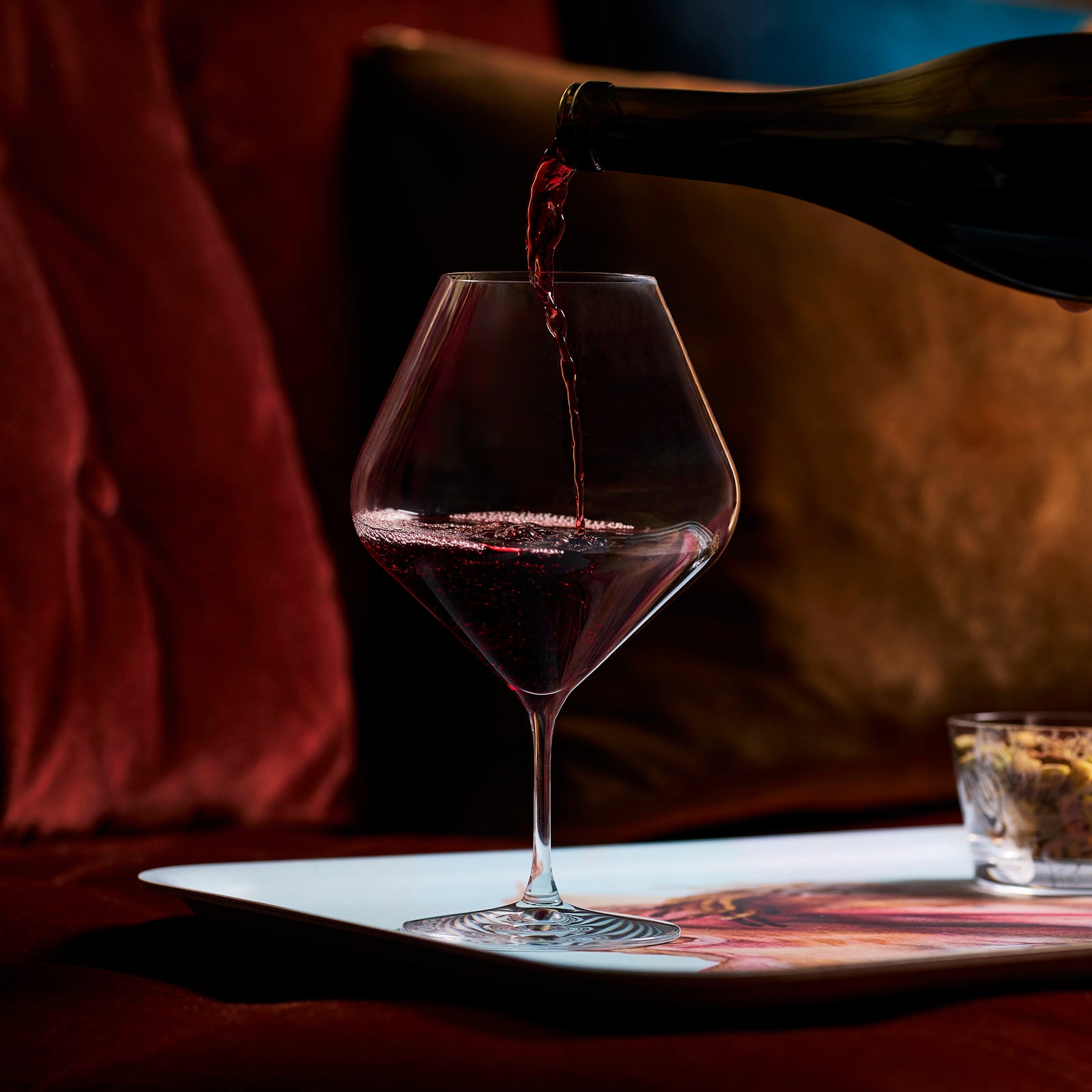 Four Caskata Library Red Wine Glasses, Set of 4, are arranged side by side; three are empty and one, featuring an oversized lead-free crystal bowl, is partially filled with red wine being gently swirled.