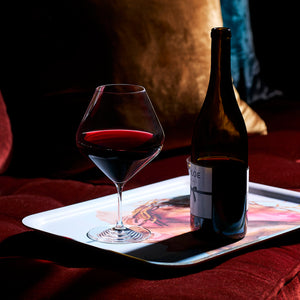 A set of four Caskata Library Red Wine Glasses, featuring lead-free crystal and oversized bowls, is displayed on a white tray with a decorative image atop red velvet with cushions in the background.