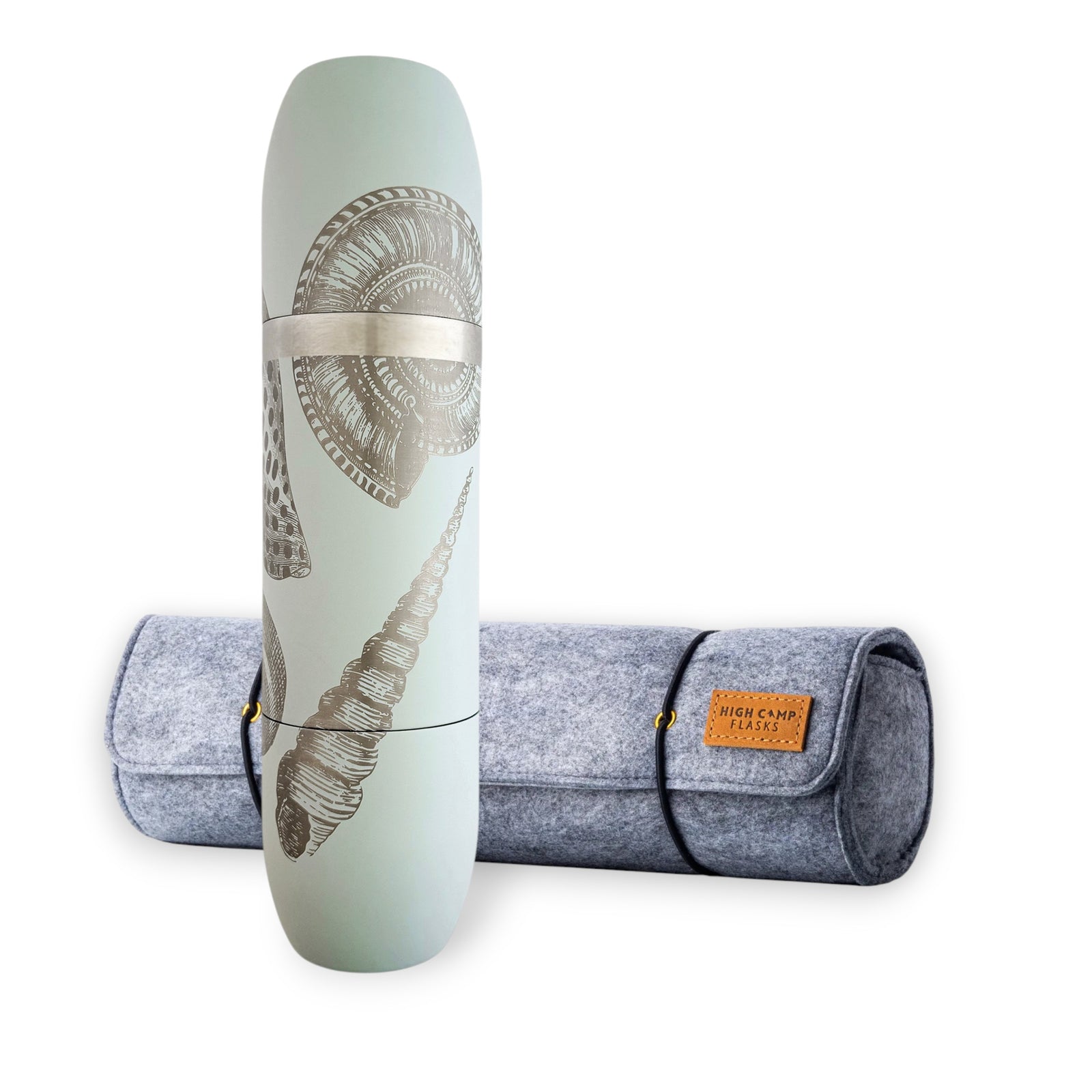 A Caskata x High Camp Light Blue Shells Wine Flask and Case Bundle stands upright next to a rolled-up gray felt carrying case with a brown leather label, the shell patterns on the flask perfectly matching your yoga mat for the ideal post-session refreshment.