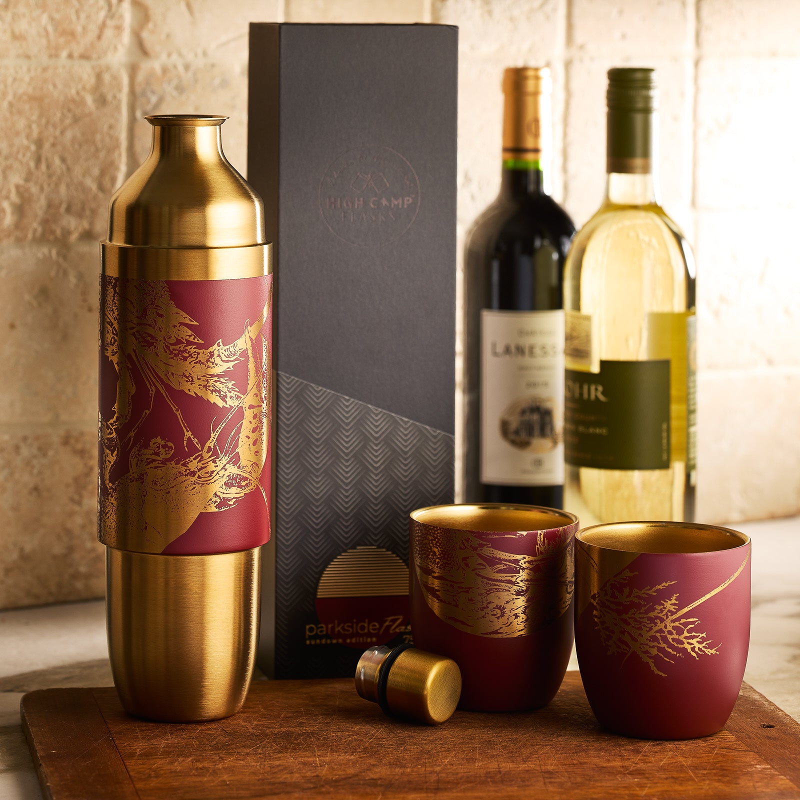 A maroon and gold insulated wine flask with a lobster motif, shown beside its black and gold box labeled "Caskata x High Camp Red Lobster Parkside Flask" by Caskata.
