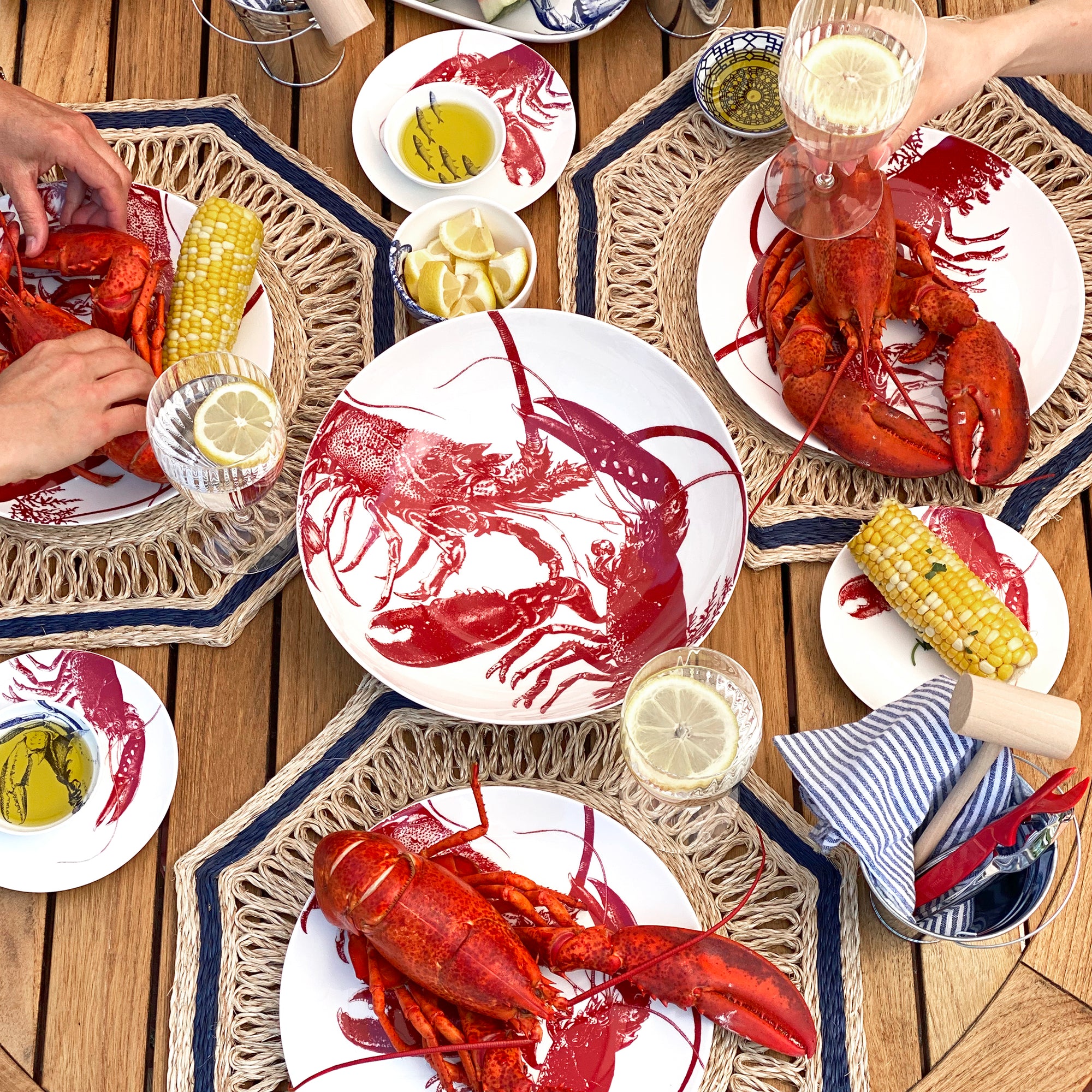 The Lobster Love Bundle by Caskata includes a set of five white plates, two napkins, and a lobster serving bowl, all featuring a striking red lobster design.
