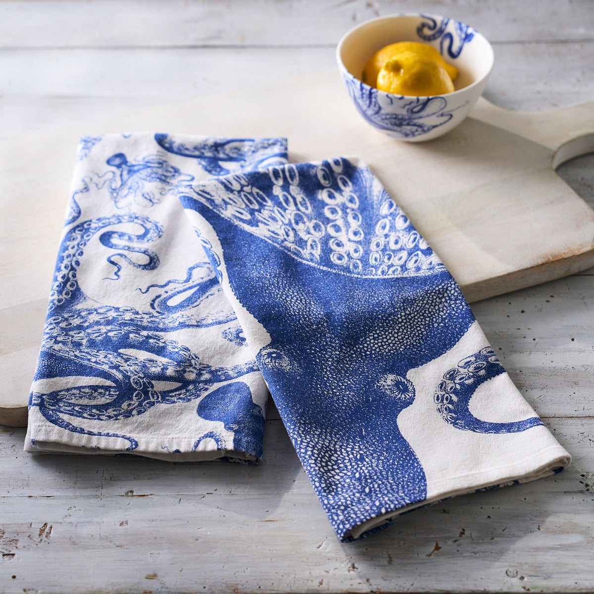 Two Lucy Kitchen Towels Set/2 by Caskata, seafaring whimsy blue and white octopus tea towels made from 100% cotton on a cutting board.