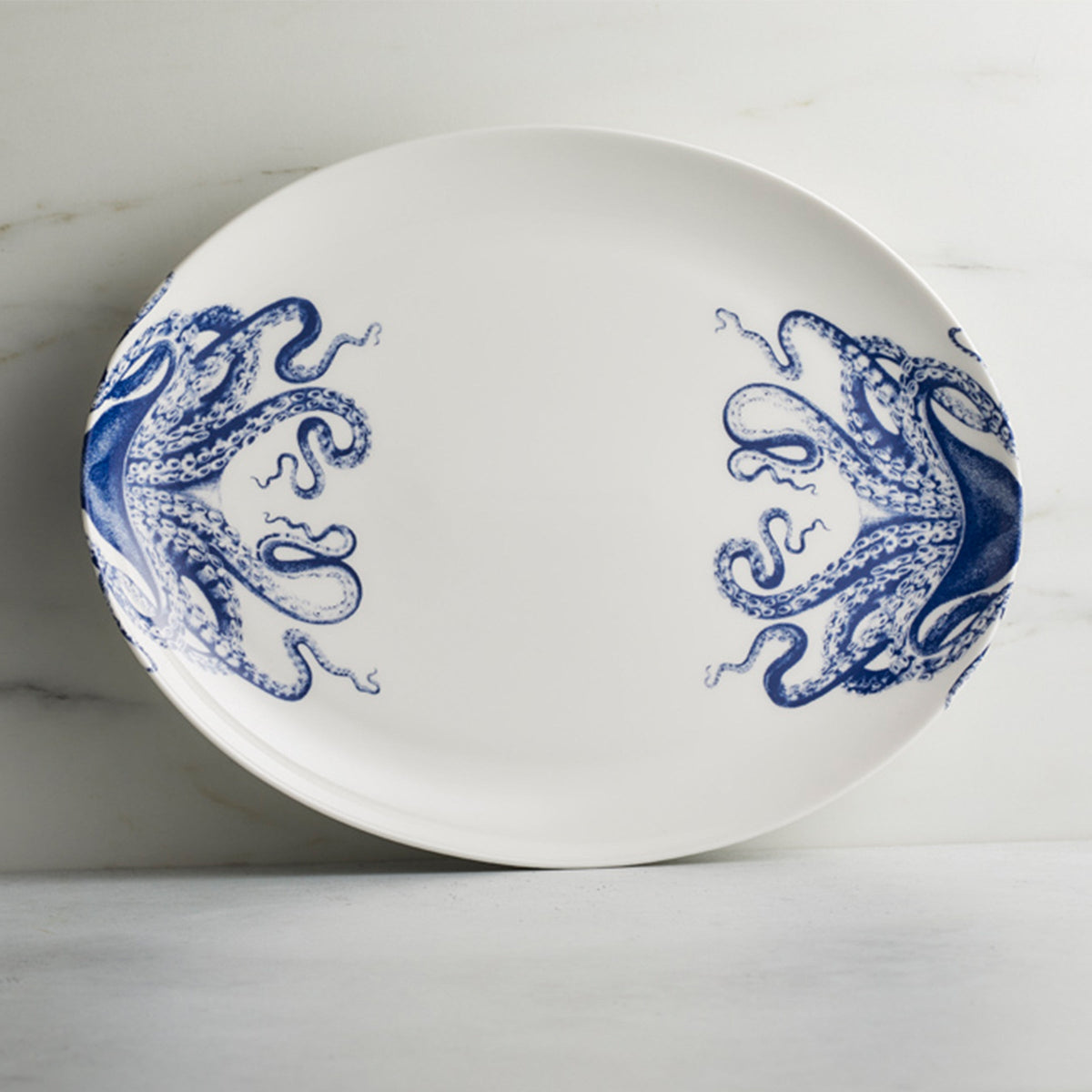 Lucy Medium Coupe Platter is a creamy white porcelain platter adorned with blue octopi wrapping around the sides.
