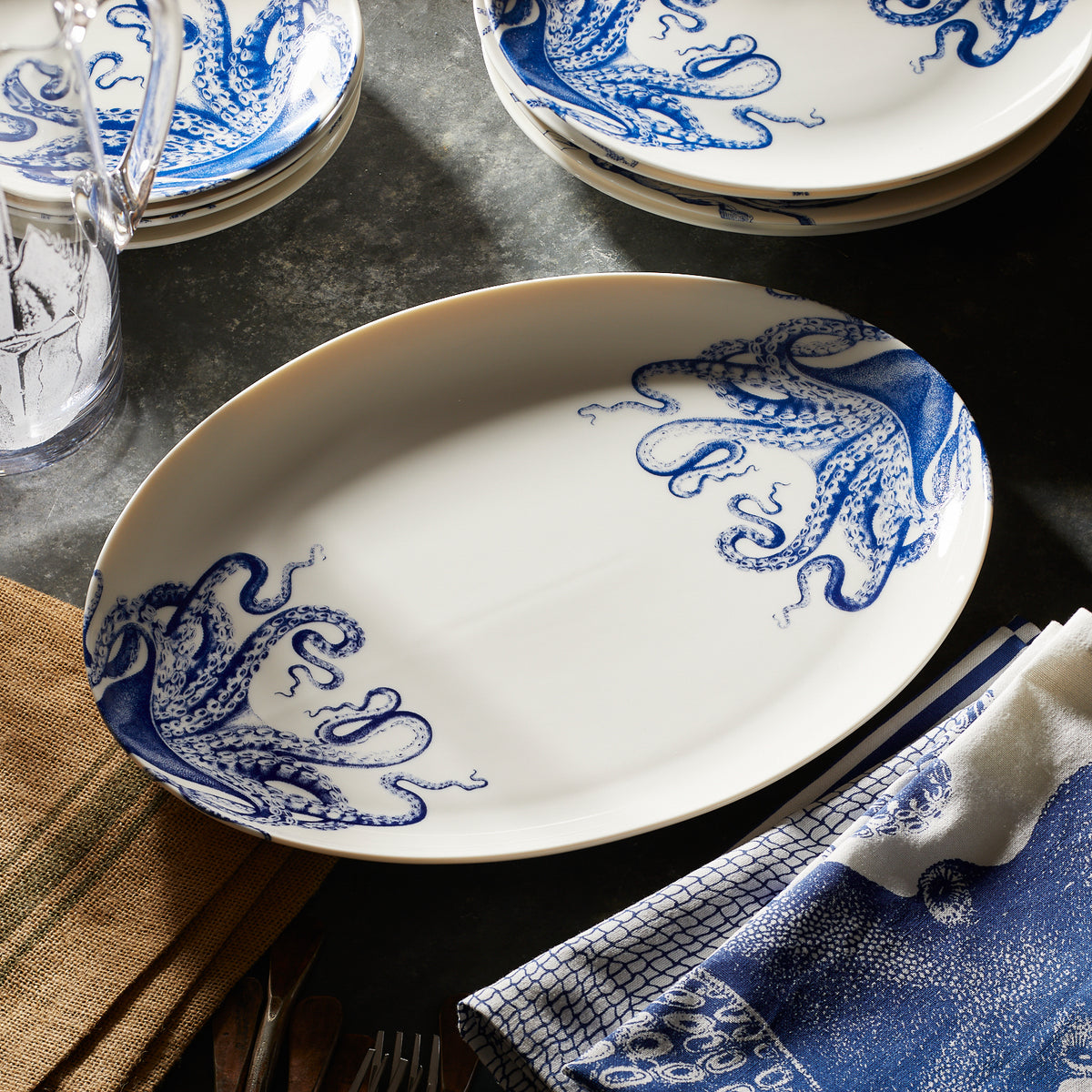 A Lucy the octopus blue and white medium coupe oval platter on a zinc table surrounded by other Lucy tableware.