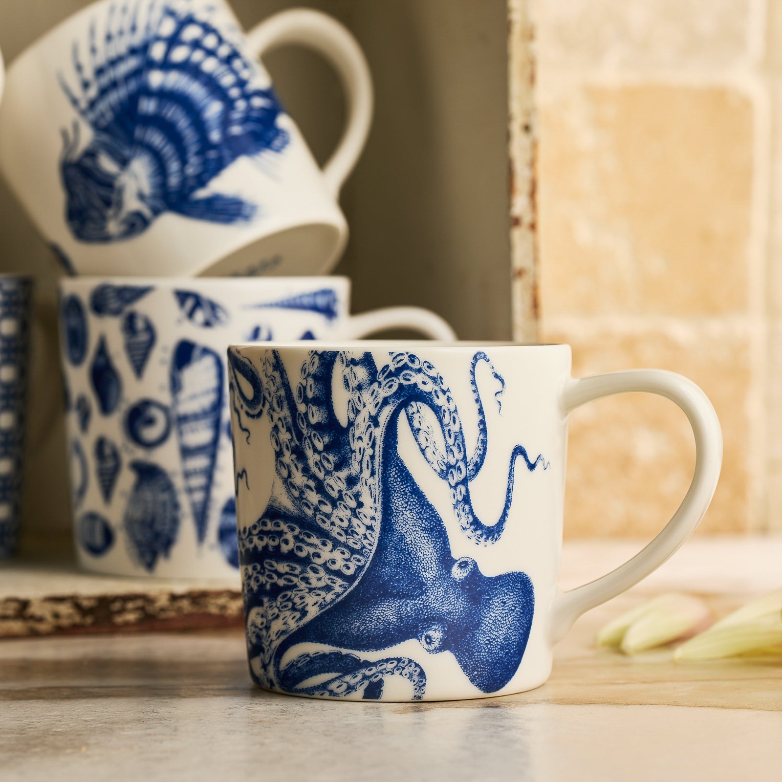 A premium porcelain Caskata Artisanal Home Lucy Mug, featuring a striking blue octopus design on the side, perfect for your morning coffee. Plus, it's dishwasher and microwave safe for added convenience.