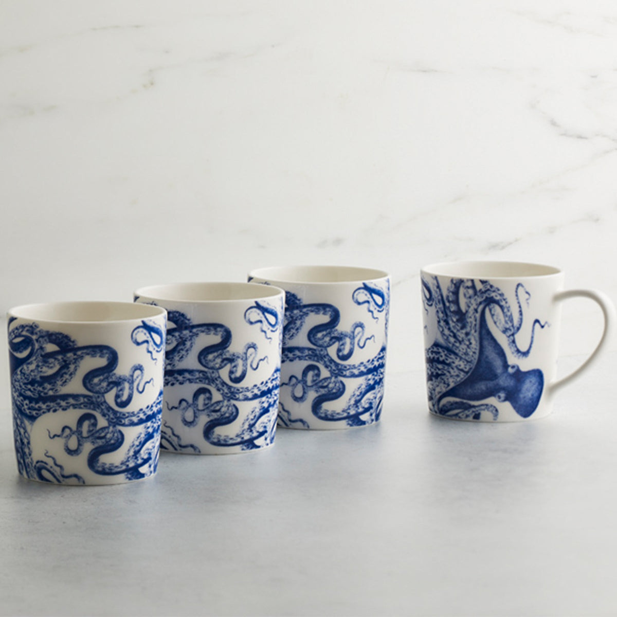 Four premium Caskata Artisanal Home Lucy Mugs with blue octopus designs arranged in a row on a light surface against a white background, both dishwasher and microwave safe.